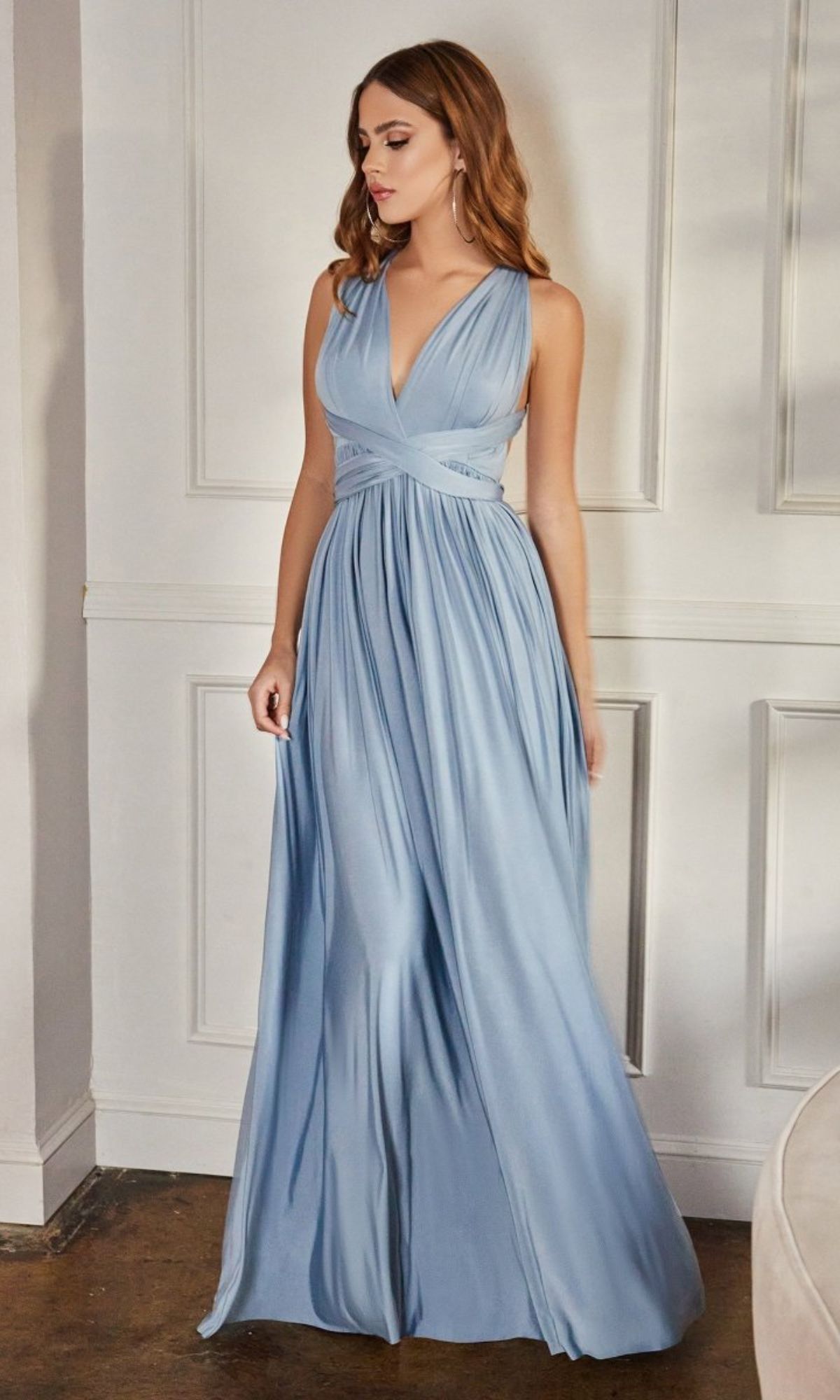 A woman models the affordable Amoris CV01 Multi-Wrap Long A-Line Prom Dress—a sleeveless, floor-length, light blue gown with a deep V-neckline—standing indoors against a white paneled wall.